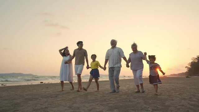 Happy big Asian family on beach holiday vacation. Multi-generation family holding hands and walking together on tropical beach at summer sunset. Family enjoy and having fun outdoor activity lifestyle.