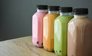 A row of various bobble tea in a plastic bottles on wooden table with black color background, copy space