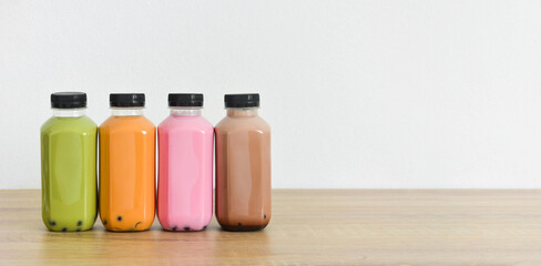 A row of various bobble tea in a plastic bottles on wooden table with white color background, copy space