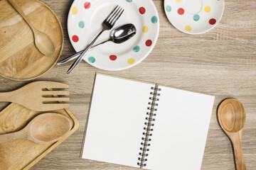 Wooden utensils, notebook and polka pot plate on a table.