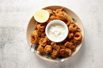 top view shot of a bowl of golden fried calamari with lemon and mayo dipping sauce