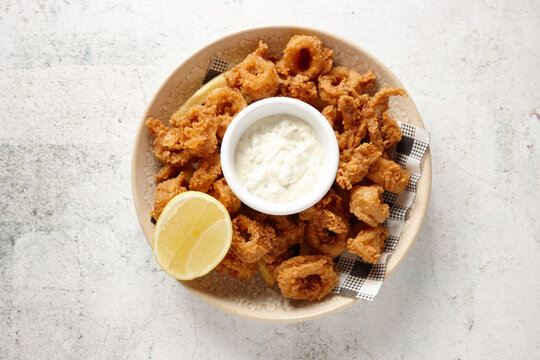 top view shot of a bowl of golden fried calamari with lemon and mayo dipping sauce