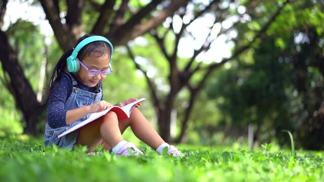 Happy asian little child girl reading a book in the garden