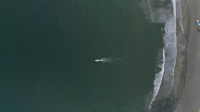 Top down aerial over lone fishing boat as it heads out to sea from beach, 4K