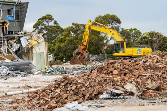 Horizontal shot of a yellow backhoe on a demolition site with a large pile of bricks