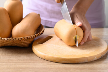 Woman hand holding kitchen knife and cutting butternut squash on wooden board for cooking