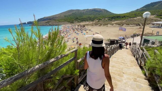 woman with white hat with her back turned down mesquida cove in mallorca balearic islands turquoise blue mediterranean sea, fine white sand beach