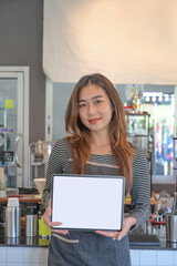 Portrait of happy waitress standing at coffee shop and showing digital tablet with empty display.