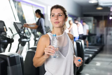 Blackout curtains Fitness Young adult sporty woman resting after fitness training in gym holding bottle with drinking water
