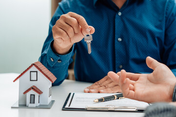 Real Estate Broker Or businessman holding white house model and house key in hand.Mortgage loan approval home loan and insurance concept.