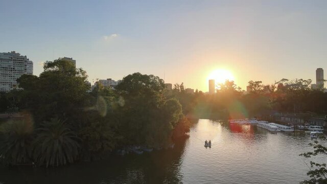 Cinematic aerial pull out shot over white greek bridge and pedal boats with sun shinning over the tranquil lake in Palermo Rose Garden at urban Parque Tres de Febrero, Buenos Aires.