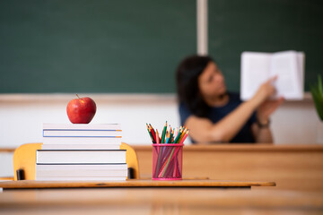 Pencils, apple and books, teacher and blackboard in the background. Education concept.