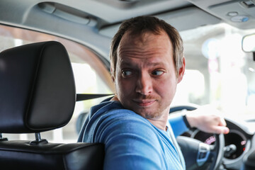 Obraz premium Blur image of the driver is driving a car. Blur photo from the salon of a man with a beard running a vehicle. A man looks away, while parking, a hand on the steering wheel.