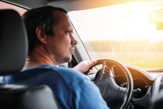 Blur image of the driver is driving a car. Blur photo from the salon of a man with a beard running a vehicle. A man looks away, while parking, a hand on the steering wheel.