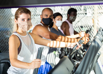Portrait of sporty young adult woman doing cardio workout exercising on elliptical cross trainer at fitness center during coronavirus outbreak