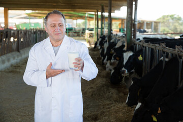 Portrait of man quality expert who is standing at the cow farm.