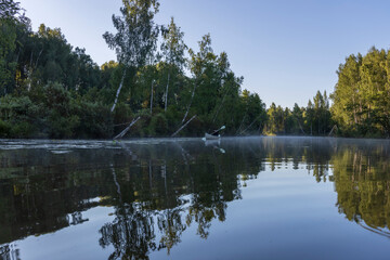 A man in a kayak floats down the river. Picturesque landscape in the morning on the river. The sun's rays touch the treetops. Kayaking early in the morning on a calm river in the summer.