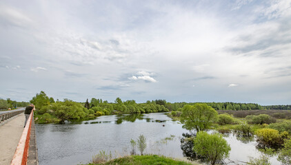 Fototapeta premium Landscape with a dramatic sky reflected in the river. Early spring, juicy May greens. Bright green foliage on trees and bushes.