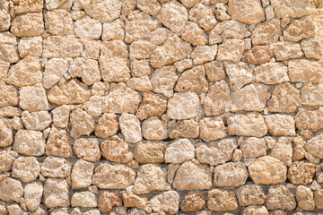 Texture oа a sandstone blocks wall. Sunlight illuminates the orange stone background. Part of a stone wall. Fossilized coral and sand stones.