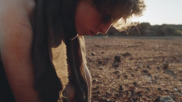 Handheld camera shot of young woman in worn dirty clothes looking at her reflection in piece of broken mirror found in post apocalyptic world