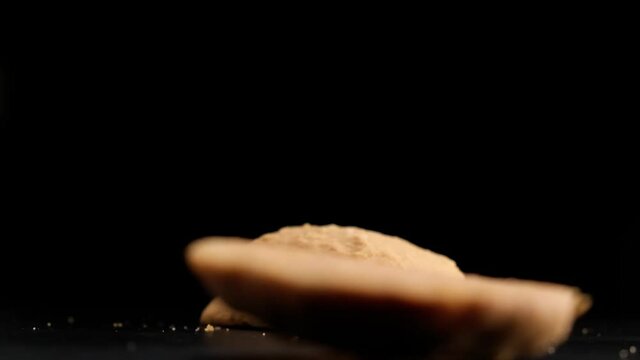 Super slow motion of stack of cookies falling on table on black background.