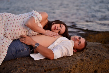 A young beautiful couple in love lies on the rocks by the sea