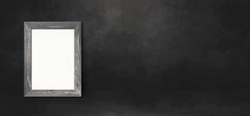 Wooden picture frame leaning on a black wall. Horizontal banner