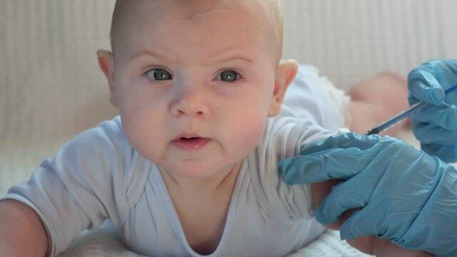 Pediatrician vaccinating newborn baby. Vaccine, Vaccination for infant child Soft focus Syringe in hands of a nurse and blurred background of infant baby on white. Doctor in blue gloves, close up.