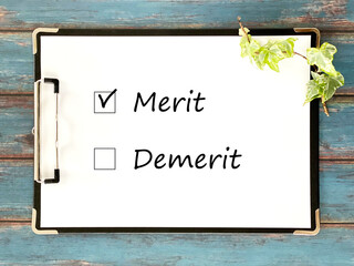クリップボードに挟んだ白い用紙_青色木板背景 _横_MeritとDemeritの文字入り