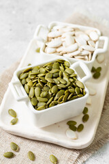 Pumpkin seeds in a white bowl on a light gray culinary background closeup	