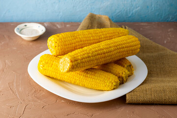 corn cooked on the cob on a white plate, next to a salt shaker with salt