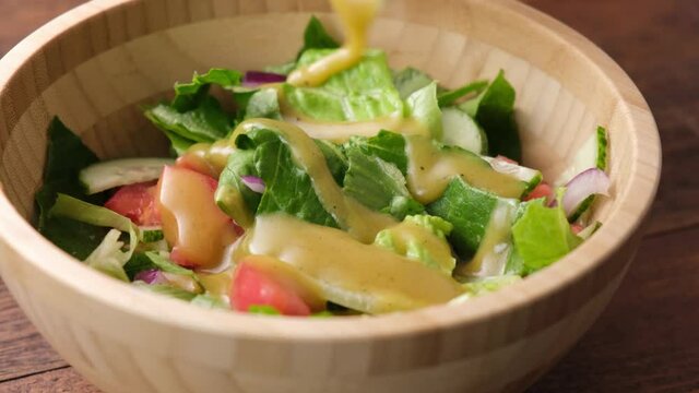 Pouring olive oil honey mustard vinaigrette on healthy salad vegetable salad in wooden bowl closeup view