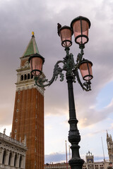 Fototapeta na wymiar Venetian lamppost with the bell tower of San Marcos in the background, in the photo there are pink storm clouds