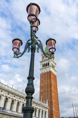 Fototapeta na wymiar Venetian lamppost with the bell tower of San Marcos in the background, with a sky full of white clouds