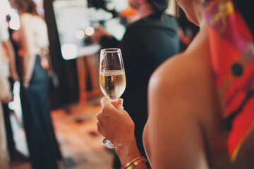 Back view woman holds misted cold glass of champagne wine in hand at party event.