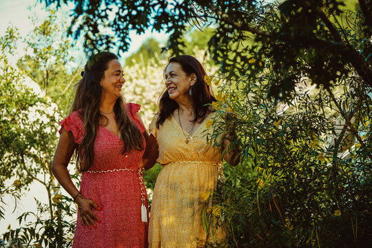 Mother and daughter looking at each other while laughing by green plants during glamping weekend