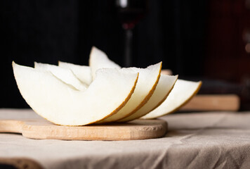 Pieces of melon on a wooden board, a glass of wine on the background. Rustic style.