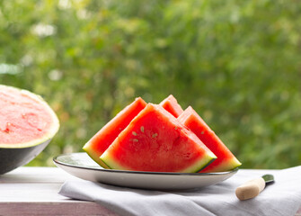 Slices of watermelon on a plate, half a watermelon in the background, outdoor. Healthy food.