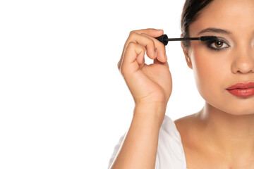 a half portrait of a young woman applies mascara