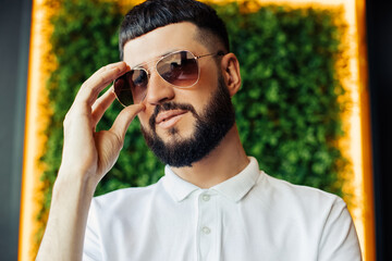 smiling man with beard, in sunglasses and white shirt, portrait of a young man smiling while looking at camera