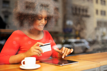 African woman in cafe makes a purchase on the Internet. Beautiful woman with digital tablet and...