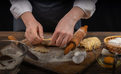 Women's hands, flour and dough. A woman in an apron cooking dough for homemade baking, a rustic home cozy atmosphere, a dark background with unusual lighting.