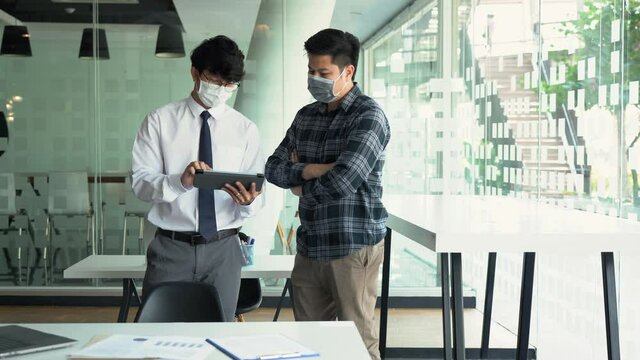Asian colleague stood at the office and analyzed corporate data while wearing a face mask during COVID-19.
