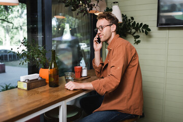 young man in glasses talking on smartphone in cafe