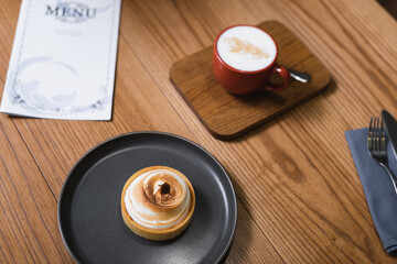 high angle view of tasty lemon tart and cappuccino near menu on wooden table