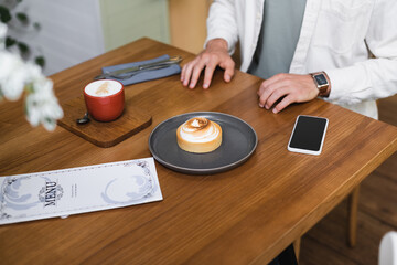 Fototapeta na wymiar cropped view of man near lemon tart, cappuccino, menu and smartphone with blank screen on table