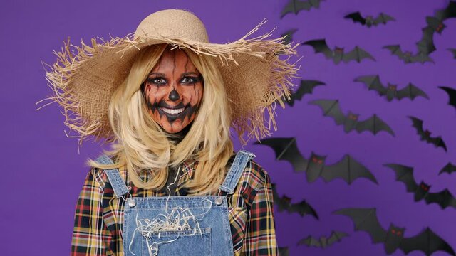 Scary bright young woman with Halloween makeup mask wears straw hat scarecrow costume looking camera nodding isolated on plain dark purple background studio portrait. Celebration holiday party concept
