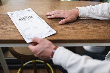 cropped view of young man taking menu in cafe