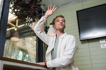 low angle view of curly man with raised hand calling waiter in cafe