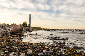 Tahkuna lighthouse on the coast during sunset at Hiiumaa, Estonia, Europe. White lighthouse with red top on the rocky beach. Sun is setting near lighthouse on the shore.